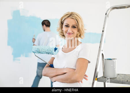 Porträt der Frau hält Farbroller mit Mann Malerei Wand im Hintergrund Stockfoto
