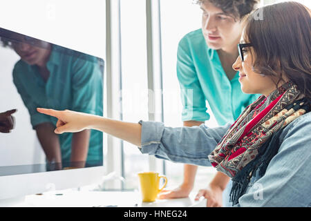 Kreative Geschäftsfrau zeigt etwas an Kollegen auf Desktop-Computer im Büro Stockfoto