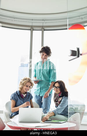 Lächelnde kreative Unternehmer diskutieren über Laptop im Büro Stockfoto