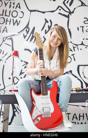 Porträt von Teenager-Mädchen mit e-Gitarre sitzend am Schreibtisch zu Hause Stockfoto