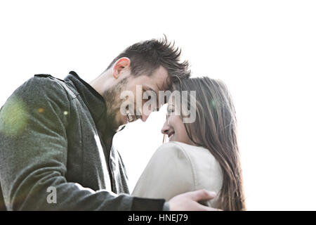 Lächelnd junger Mann und Frau gegen klaren Himmel umarmen Stockfoto