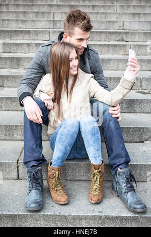 Volle Länge des jungen Paares unter Bild von sich selbst auf Schritte im freien sitzend Stockfoto