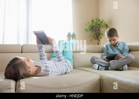 Geschwister, die mit Technologien zu Hause auf sofa Stockfoto