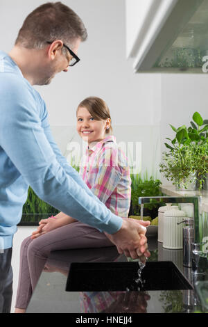 Lächelndes Mädchen Blick auf Vater Händewaschen in Küche Stockfoto