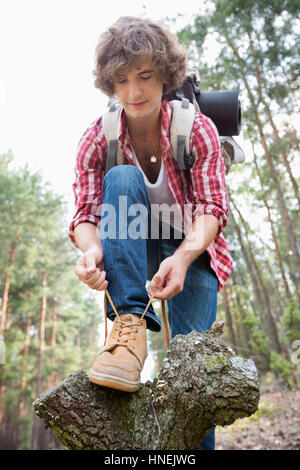 Voller Länge der männlichen Backpacker, die Schnürsenkel zu binden, im Wald Stockfoto