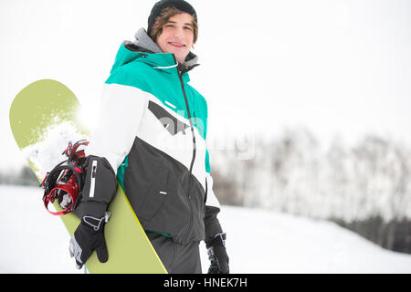 Porträt von hübscher junger Mann mit Snowboard im Schnee Stockfoto