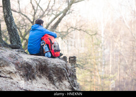 Rückansicht des Wanderer mit Rucksack sitzt am Rand der Klippe im Wald Stockfoto