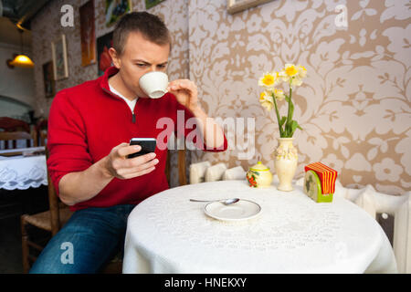 Mann mit Kaffee beim Lesen von SMS auf Handy im café Stockfoto