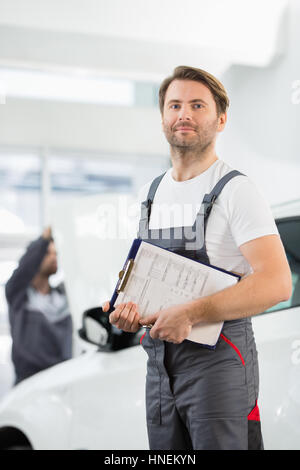 Porträt von zuversichtlich männliche Automechaniker mit Zwischenablage in Auto-Reparatur-Speicher Stockfoto