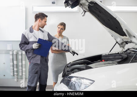 Junge männliche Mechaniker erklärt Automotor Kundin in Kfz Werkstatt Stockfoto