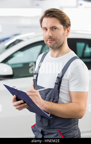 Porträt des zuversichtlich Kfz Mechaniker Schreibens auf Zwischenablage in Werkstatt Stockfoto