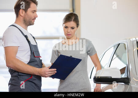 Mechaniker, die Zwischenablage zu halten, während im Gespräch mit weiblichen Kunden in Werkstatt Stockfoto