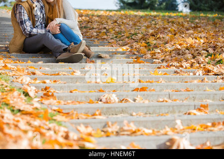 Niedrige Abschnitt des Paares sitzen auf Stufen im Park im Herbst Stockfoto