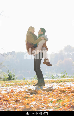 Junger Mann heben Frau im Park im Herbst Stockfoto