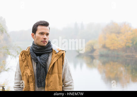 Nachdenklicher junger Mann in warme Kleidung stehend gegen See Stockfoto