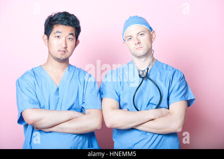 Porträt von zwei männlichen Chirurgen stehen mit verschränkten über rosa Hintergrund Stockfoto
