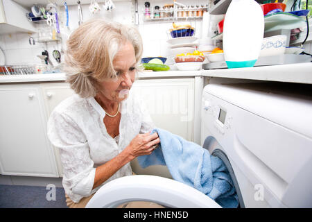 Ältere Frau, die Waschmaschine zu Hause laden Stockfoto