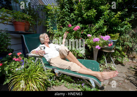 Ältere Frau mit Weinglas auf Liegestuhl im Garten entspannen Stockfoto