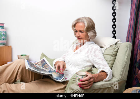 Ältere Frau liest Zeitung beim Entspannen zu Hause Stockfoto