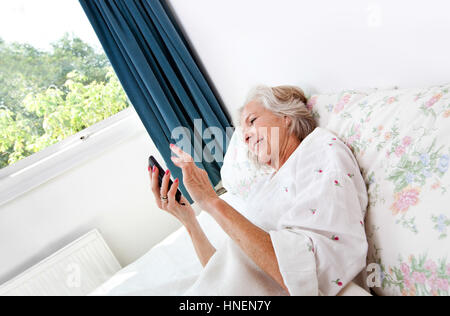 Glückliche ältere Frau mit Handy im Bett zu Hause Stockfoto