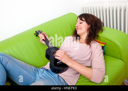 Junge Frau auf Couch spielt ukulele Stockfoto