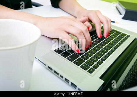 Nahaufnahme eines Womans Hände Tippen auf Laptop mit Becher im Vordergrund Stockfoto