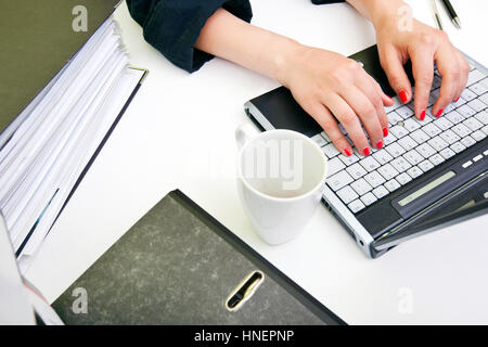 Nahaufnahme eines Womans Hände Tippen auf Laptop mit Ordnern und Becher Stockfoto