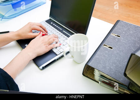 Nahaufnahme eines Womans Hände Tippen auf Laptop mit Ordnern und Becher Stockfoto