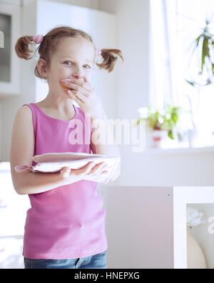 Junges Mädchen essen Kuchen in Küche Stockfoto