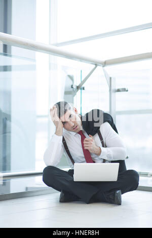 Gestresst Geschäftsmann auf Boden arbeiten am Laptop sitzend Stockfoto