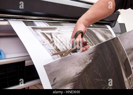 Professionelle Mann Hand abschneiden mit der Schere Bilder gedruckt auf Papierrollen mit professionellen Breitformat-Drucker Stockfoto