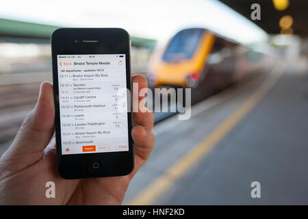 BRISTOL, UK - 8. April 2014: Eine männliche Hand, die ein iPhone am Bahnhof Bristol mit einem Zug im Hintergrund. Das Smartphone zeigt live tr Stockfoto