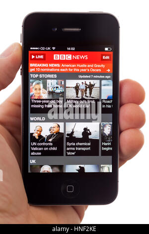 BATH, Großbritannien - 16. Januar 2014: Eine Hand mit einem Apple iPhone 4 s Anzeigen der ersten Seite von der BBC-News-App auf einem weißen Hintergrund. Die app kann Stockfoto