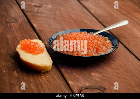 roter Kaviar in einer blauen Platte. Holzbohlen. Sandwich mit Butter und Kaviar Stockfoto