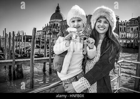 Eine andere Welt Urlaub. Porträt von glücklich moderne Mutter und Kind Reisende am Ufer in Venedig venezianischen Maske mit gedrückter Stockfoto