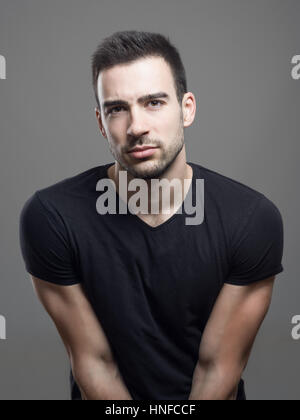 Stimmungsvolle Porträt Fit muskulös ernster Mann mit leeren schwarzen T-shirt, Blick in die Kamera verdächtig über graue Studio-Hintergrund. Stockfoto