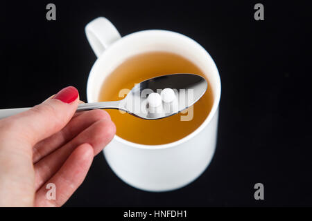 Hand mit einem Löffel mit Süßstoff mit einer Tasse Tee im Hintergrund Stockfoto