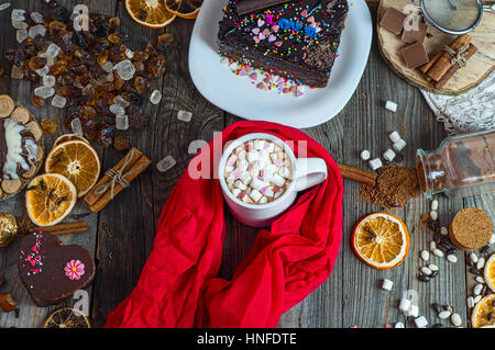 Tasse Schokolade Getränk mit Marshmallows gehüllt in rot Textil Schal auf dem Tisch eine Menge Süßigkeiten und Bonbons, Ansicht von oben Stockfoto