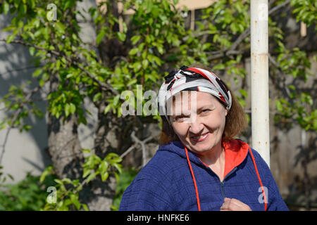 Close-up im freien Kopf und Schultern Porträt des gealterten lächelnde Frau in hellem Sonnenlicht auf grünen Blättern Hintergrund. Stockfoto