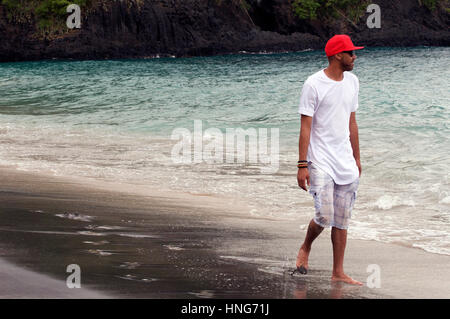 Cooler Typ Spaziergänge entlang Sandy Beach in Bali Indonesien tragen rote Baseballkappe, weißes T-Shirt und kurze Hosen Stockfoto