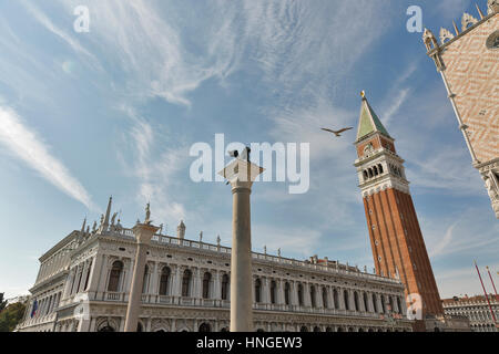 Möwe fliegt über Spalten mit Skulpturen vor Dogenpalast und Campanile am St Markusplatz in Venedig, Italien. Stockfoto