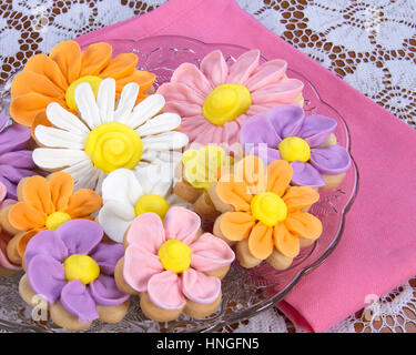 Ausgefallene hausgemachte Frühlingsblumen Zucker Cookies mit königlicher Zuckerglasur Blütenblätter auf geleitet. Serviert auf einem Glas Platte weißer Spitze Tuch rosa Serviette Stockfoto