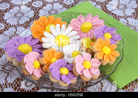 Ausgefallene hausgemachte Frühlingsblumen Zucker Cookies mit königlicher Zuckerglasur Blütenblätter auf geleitet. Auf ein Glas Platte weißer Spitze Tabelle grün Stoffserviette serviert Stockfoto