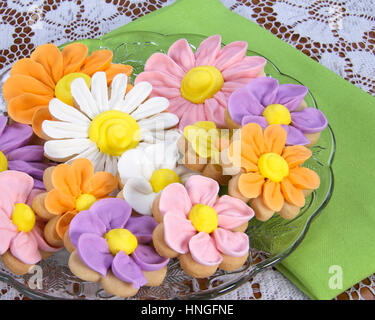 Ausgefallene hausgemachte Frühlingsblumen Zucker Cookies mit königlicher Zuckerglasur Blütenblätter auf geleitet. Auf ein Glas Platte weißer Spitze Tabelle grün Stoffserviette serviert Stockfoto