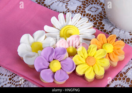 Schickes elegantes hausgemachte Frühlingsblumen Zucker Cookies mit königlicher Zuckerglasur Blütenblätter verrohrt auf serviert auf einer rosa Serviette auf Tisch mit weißer Spitze Tischdecke und Stockfoto