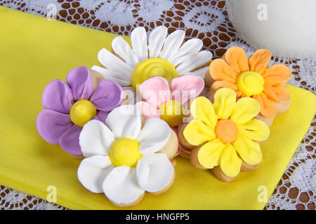 Schickes elegantes hausgemachte Frühlingsblumen Zucker Cookies mit königlicher Zuckerglasur Blütenblätter verrohrt auf serviert auf einer gelben Serviette auf Tisch mit weißer Spitze Tischdecke ein Stockfoto