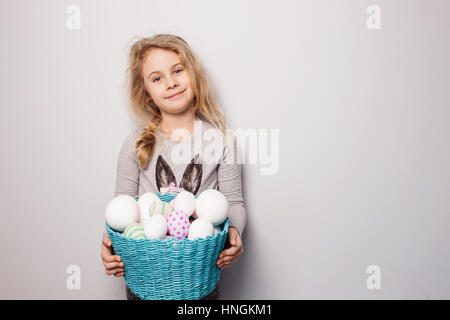 Kleine blonde Mädchen hält Korb mit bemalten Eiern. Ostern-Tag. Stockfoto