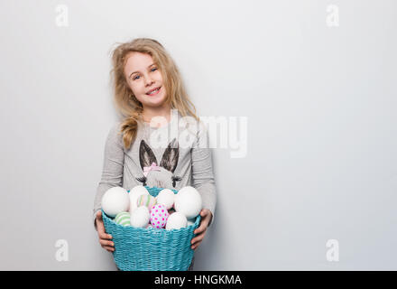 Kleine blonde Mädchen hält Korb mit bemalten Eiern. Ostern-Tag. Stockfoto