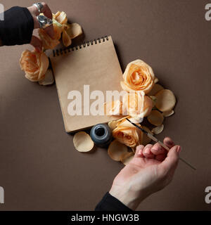 Weibliche Hand aufschreiben auf Briefpapier mit Blumen auf den Tisch Browb, Ansicht von oben Stockfoto