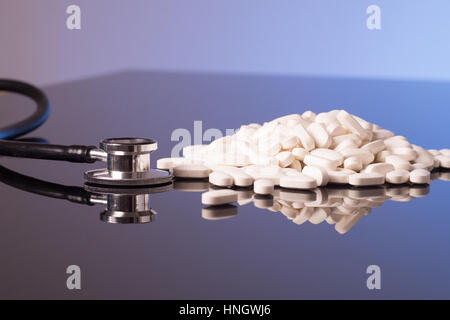 Ein Haufen weißen Pillen und Stethoskop ist auf einem glänzend schwarzen blauen Hintergrund isoliert. Stockfoto
